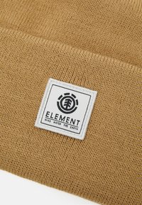 Brązowa dzianinowa czapka z teksturowanym wzorem i białą prostokątną naszywką z logo "ELEMENT" oraz słowami "WIATR WODA OGIEŃ ZIEMIA."