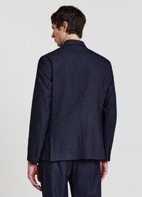 Marineblauer strukturierter Blazer mit einem einzelnen Schlitz, Revers mit Kerbe und geknöpften Manschetten, kombiniert mit passenden Hosen, von hinten gesehen.