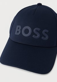 Tmavomodrá šiltovka z textúrovanej látky s veľkým reliéfnym logom "BOSS" na prednom paneli. Zakrivený tvar štítku.