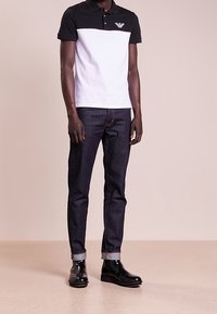 Svart och vit färgblockerad pikétröja med korta ärmar, kombinerad med mörka jeans och svarta ankelstövlar. Ikonisk logotyp på bröstet.