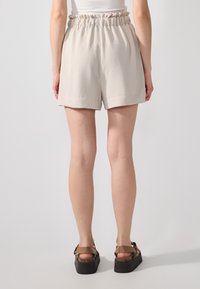 Shorts beige clair avec une taille élastique à volants, fabriqués dans un tissu texturé, présentant une coupe décontractée et une longueur mi-cuisse.