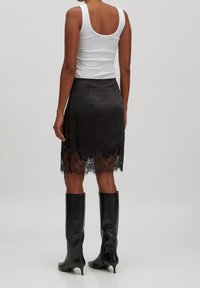 Jupe en satin noir avec un ourlet en dentelle présentant des motifs floraux complexes. Associée à un débardeur blanc et des bottes noires montantes jusqu'au genou.