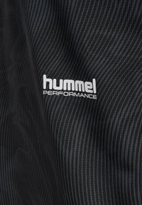 Czarna teksturowana tkanina z nadrukowanym na powierzchni białym logo „hummel PERFORMANCE”.
