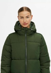 Groene puffy jas met een kap, voorzien van een ritssluiting aan de voorkant en elastische koordjes, gemaakt van waterafstotend materiaal met een gestructureerde afwerking.