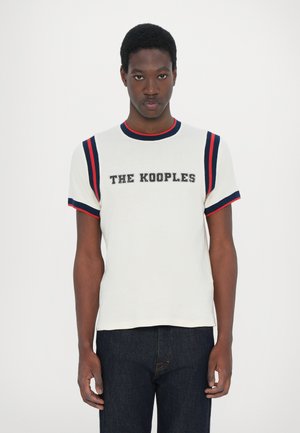 Balta kokvilnas T -krekls ar sarkaniem un jūras zilās krāsas svītrojumiem uz piedurknēm, ar izteiktu "THE KOOPLES" logo biezā burtu fontā uz krūšu daļas.