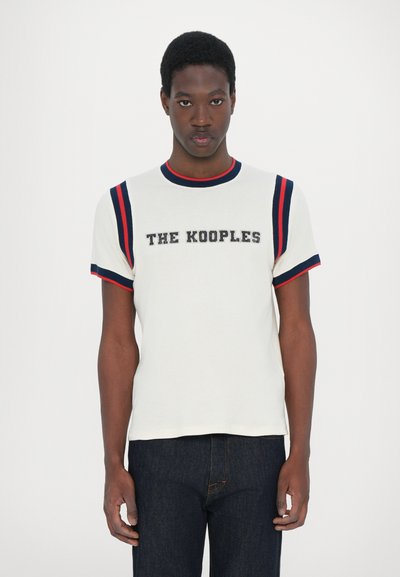 Fehér pamut póló piros és sötétkék csíkos részletekkel a ujjakon, amelyen "THE KOOPLES" felirat szerepel vastag betűkkel a mellkason.