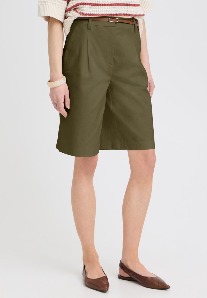 Femme portant un short olive jusqu'aux genoux avec une ceinture fine marron, un pull rayé, un bracelet beige et des ballerines marron à bout pointu.