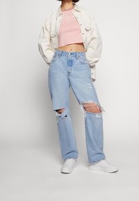 Jeans azzurri chiari con strappi ampi, abbinati a un top corto rosa e a una giacca oversize color avorio. Sneakers bianche completano il look.