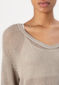 Helle beige Strickjacke mit lockerem, offenem Maschenbild. Verfügt über einen weiten Halsausschnitt und strukturierte Rippbündchen. Zeigt einen lässigen, oversized Stil.