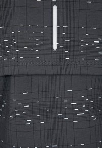 T-shirt de sport gris avec un motif en grille et des lignes blanches, accompagné de subtils accents. Le tissu semble lisse et extensible, conçu pour les activités sportives.