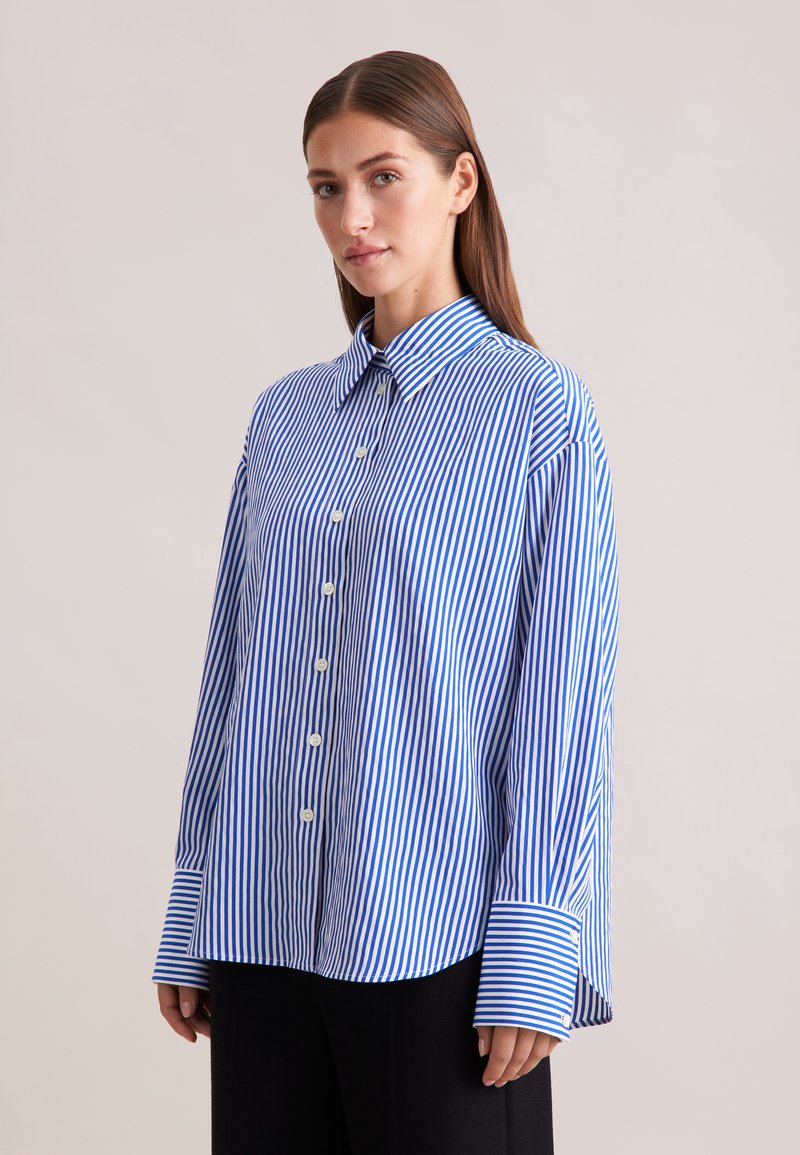 Camicia over-size a righe blu e bianche con colletto button-down e polsi larghi, realizzata in un tessuto morbido e dal fit rilassato.