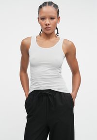 Biały dopasowany top na ramiączkach o szerokich paskach, zestawiony z czarnymi spodniami z elastycznym pasem. Gładki materiał o klasycznym kroju i bez wzorów.