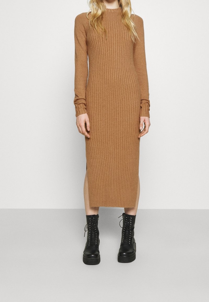 Gehaakt langzichtig jurkje in warm bruin met een ribbelstructuur, zijsplits en een getailleerd silhouet, gecombineerd met zwarte veterschoenen.