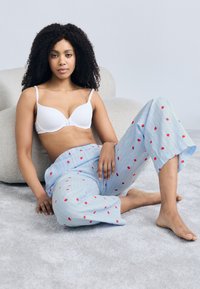 Soutien-gorge blanc et pantalon de pyjama bleu. Le pantalon est orné de motifs de fraises rouges sur un fond rayé. Le tissu semble doux et léger.