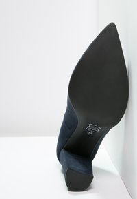 Kungsblå mocka högklackad sko med spetsig tå och en texturerad yta. Sulan är svart och skon är märkta med storlek 37.