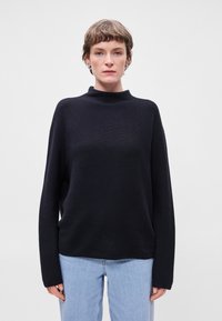 Μαύρο, πουλόβερ μακριού μανικιού με ψεύτικο γιακά, φτιαγμένο από υφασμάτινο υλικό, συνδυασμένο με ανοιχτού χρώματος, χαλαρού στυλ τζιν.