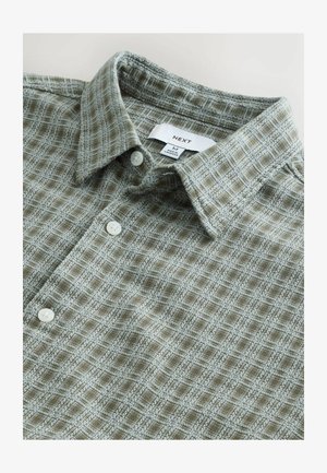 Zielona koszula w kratkę z miękką fakturą, z zapięciem na guziki i białymi guzikami. Metka widoczna wewnątrz kołnierza, rozmiar M.