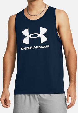 Man draagt een mouwloos tanktop van Under Armour in marineblauw en lichtgrijze korte broek, toont bovenlichaam en armen.