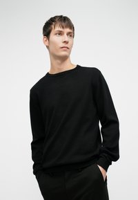 Schwarzer Strickpullover mit Rundhalsausschnitt, langen Ärmeln und gerippten Bündchen. Glatte Textur mit bequemer Passform, kombiniert mit dunklen Hosen.