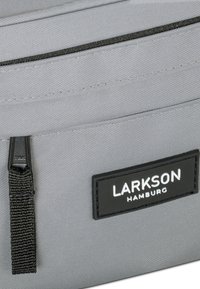 Pochette in tessuto grigio con superficie texture, multiple tasche con cerniera e un'etichetta nera con "LARKSON HAMBURG" in lettere bianche.