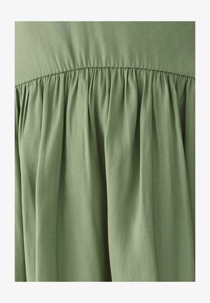 Lichtgroene stof met diagonale weefstructuur, verzameld in zachte plooien onder een gestikte naad.