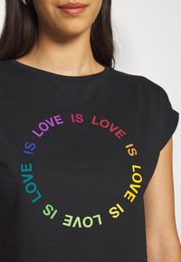 Camiseta de algodón negra con un diseño de texto en forma de arcoíris circular que dice "EL AMOR ES AMOR" en colores degradados alrededor del cuello. Manga corta.