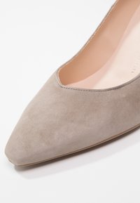 Chaussure pour femme en daim beige à bout pointu, avec un intérieur en cuir lisse et des coutures discrètes le long du bord d'ouverture.
