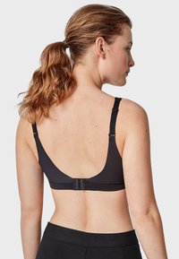 Soutien-gorge noir avec des bretelles larges, des coutures plates et une fermeture à crochets au dos. Tissu lisse avec un design minimaliste.