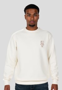 Sudadera de color crema hecha de algodón, con un diseño de personaje bordado en el pecho. Tiene cuello redondo y puños acanalados.
