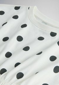 Valge kangas suurte ebaühtlaste mustade täppidega ja ümar kaelus, näidates osa rõivastuse ülemisest osast.