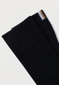 Fekete kötött zokni bordázott textúrával, a szár felső részén fehér és arany csíkkal. Az anyag lágy és tartós hatású.