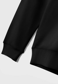 Felpa nera con polsini e orlo a costine, realizzata in un tessuto morbido e liscio. Il design è semplice, senza motivi o accessori visibili.