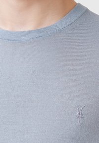 Maglione a maglia azzurro chiaro con colletto rotondo, caratterizzato da un logo ricamato discreto sul lato sinistro. Texture morbida e design aderente.