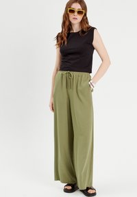 Haut sans manches noir associé à un pantalon large olive. Détails notables : taille élastique, poches et sandales noires.