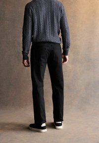 Sz�ürke mintás kötött pulóver, fekete nadrág és fekete sportcipő fehér talppal; hátulról nézve, semleges háttér előtt.