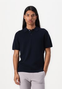 Navy strukturierte Kurzarm-Polo-Shirt mit Kragen, Drei-Knopf-Leiste und gerippten Bündchen, kombiniert mit hellgrauen Hosen.