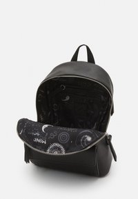 Czarny skórzany mini plecak z otwartym zamkiem błyskawicznym, odsłaniający wewnętrzną podszewkę ozdobioną wzorami kosmicznymi i niebieskimi.