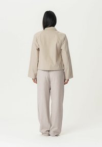 Beige lyhytnenä takki, jossa on kaulus, pitkät hihat ja sileä pinta, yhdistettynä vaaleanharmaisiin leveälahkeisiin housuihin.