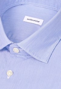 Chemise bleu clair à fines rayures blanches, un bouton blanc près du col et une étiquette de la marque Seidensticker à l'intérieur du col.