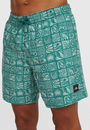 Tyrkysové plavkové šortky s bielymi tropickými a geometrickými vzormi, elastickým pásom so sťahovacou šnúrkou, nosené osobou s tmavou pokožkou.