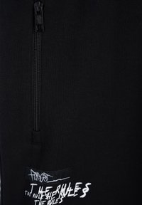 Czarna hoodie na zamek błyskawiczny z miękką fakturą materiału, z białym tekstem graficznym z przodu i małą metką przy dolnym brzegu.