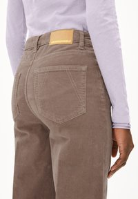 Bruine corduroy broek met een gestructureerde afwerking, voorzien van achterzakken en een tan leren label met het opdruk "ARMEDANGELS".