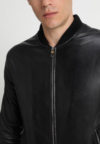 Zwarte leren bomberjack met een geribbeld kraag, voormezip sluiting en een gladde textuur. Heeft een minimalistisch ontwerp.