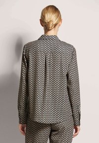 Langärmliges Hemd in Schwarz mit einem Rautenmuster in Creme. Verfügt über einen Kragen, knöpfbare Manschetten und eine kastige Passform mit einer Falte auf der Rückseite.