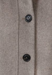 Manteau en laine beige clair avec une texture douce, doté de deux boutons noirs à l'avant et d'une coupe droite et ajustée.