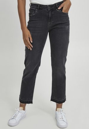 Black denim jeans with a straight-leg fit, featuring distressed patches and frayed hems, paired with white sneakers.