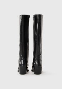 Bottes noires jusqu'aux genoux en cuir lisse, avec un léger talon et une fermeture éclair visible à l'arrière pour un enfilage facile.