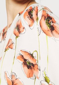 Kwiatowa sukienka z białym tłem, na którym znajdują się duże nadruki maków w odcieniach różu i pomarańczu, zielone łodygi oraz dekolt w kształcie litery V. Tekstura wydaje się gładka.