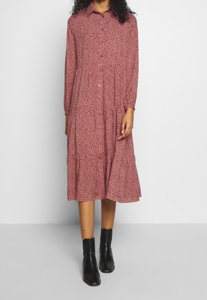 Červené midi šaty s puntíky, s knoflíkovým zapínáním vpředu, dlouhými rukávy a vrstvenou sukní. Vyrobeno z lehké látky; doplněno černými kotníkovými botami.