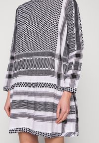 Vestido de patrones en blanco y negro con mangas tres cuartos, que presenta diseños geométricos y rayas variadas, hecho de una tela liviana.